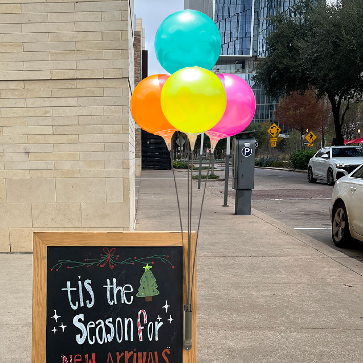 Reusable balloon cluster with 4 colorful balloons attached to an A-Frame Sign in front of a small business. 